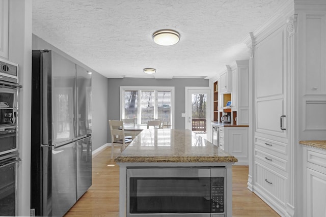 kitchen with light stone counters, white cabinetry, appliances with stainless steel finishes, and light wood finished floors