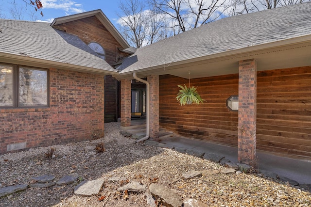 entrance to property featuring brick siding and roof with shingles