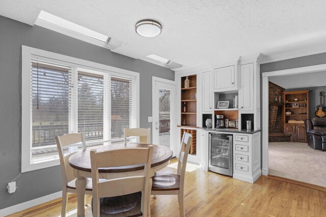 dining room featuring wine cooler, a textured ceiling, a bar, and light wood-type flooring