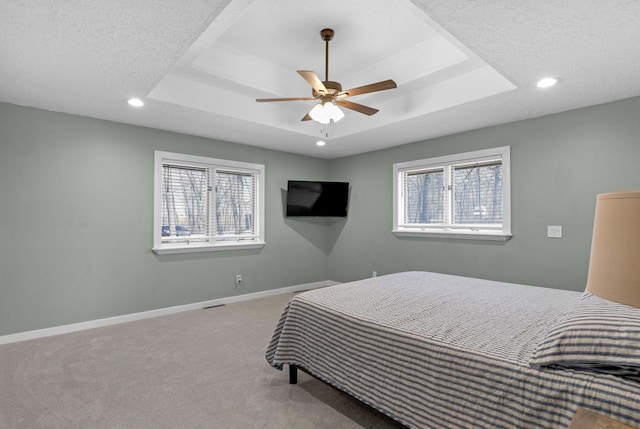 carpeted bedroom featuring multiple windows, baseboards, and a tray ceiling