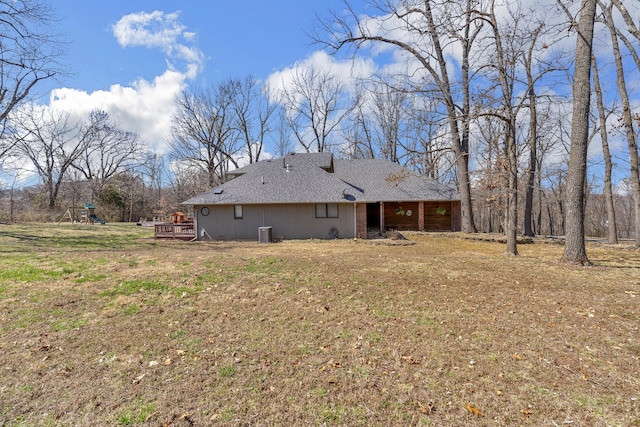 back of house featuring a playground, a lawn, central AC, and a shingled roof