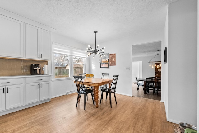 dining room with a notable chandelier, visible vents, light wood finished floors, and a textured ceiling