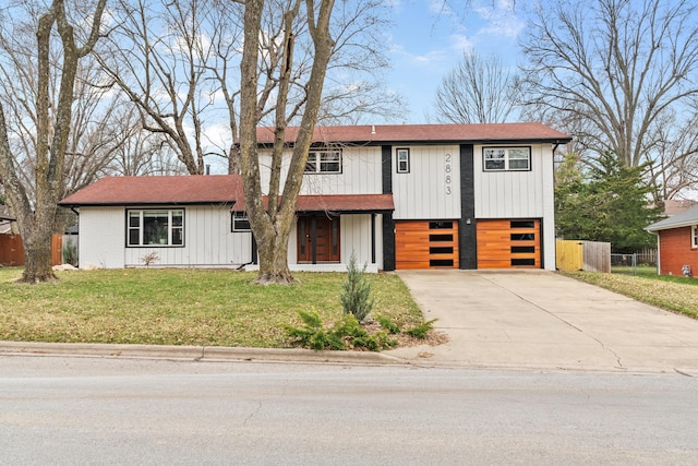 view of front facade featuring a front lawn, fence, board and batten siding, and driveway