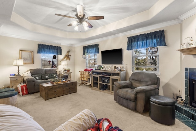 carpeted living area featuring a raised ceiling, crown molding, a fireplace, and ceiling fan