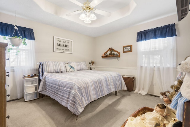 bedroom featuring a tray ceiling, carpet flooring, visible vents, and ceiling fan