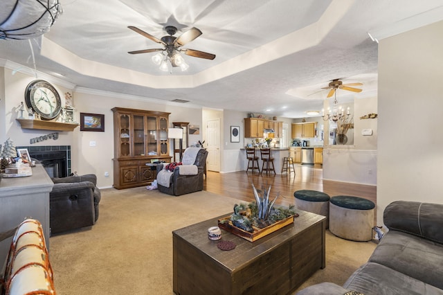 living area with light carpet, a ceiling fan, a tray ceiling, a fireplace, and crown molding