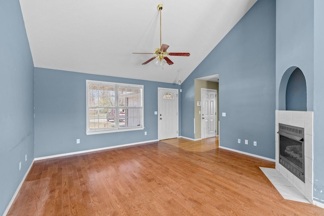 unfurnished living room with baseboards, a tiled fireplace, wood finished floors, high vaulted ceiling, and a ceiling fan