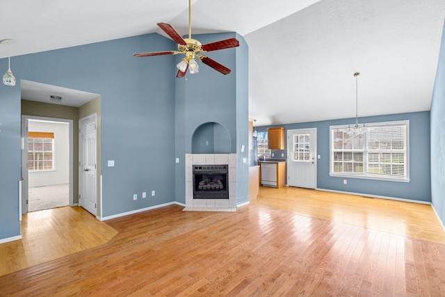 unfurnished living room featuring a tiled fireplace, a healthy amount of sunlight, light wood-style floors, and a ceiling fan