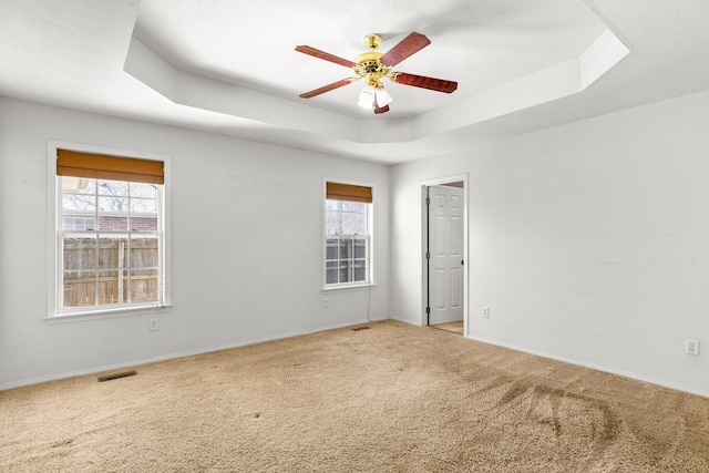 empty room with visible vents, plenty of natural light, a raised ceiling, and ceiling fan