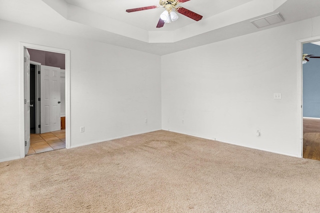 spare room with a tray ceiling, carpet floors, visible vents, and ceiling fan