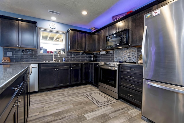 kitchen with visible vents, a sink, backsplash, dark stone counters, and appliances with stainless steel finishes