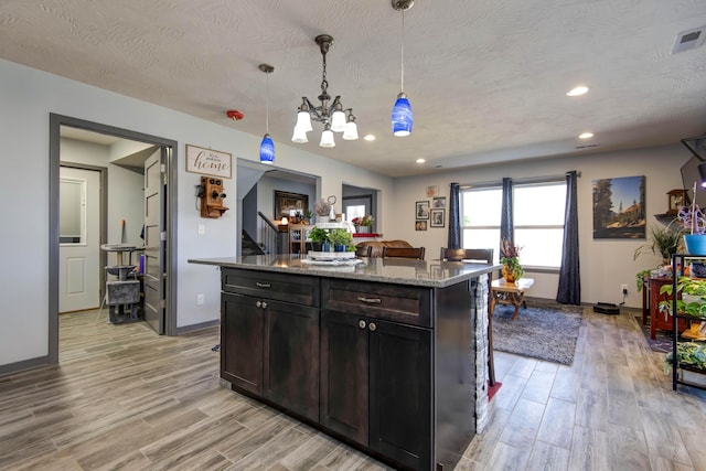 kitchen with light stone countertops, visible vents, an inviting chandelier, pendant lighting, and light wood-type flooring