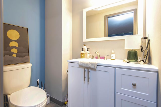 half bathroom with baseboards, toilet, and vanity