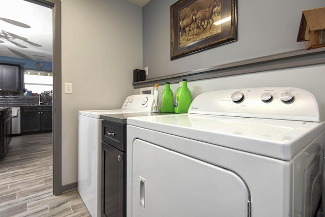 washroom featuring baseboards, cabinet space, a sink, light wood-style floors, and washing machine and dryer