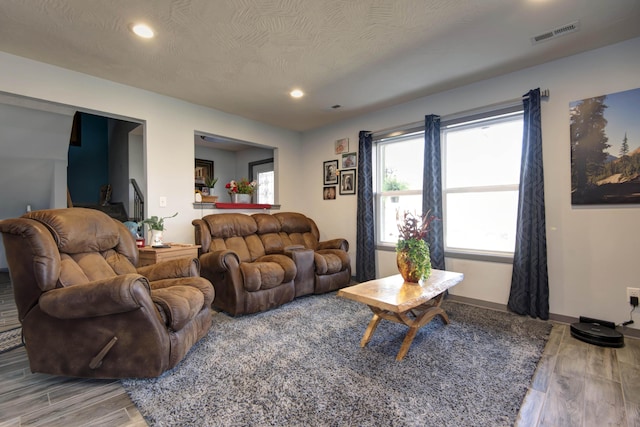 living area featuring visible vents, baseboards, recessed lighting, light wood-style floors, and a textured ceiling