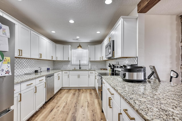 kitchen with white cabinets, stainless steel appliances, light wood-style floors, and a sink