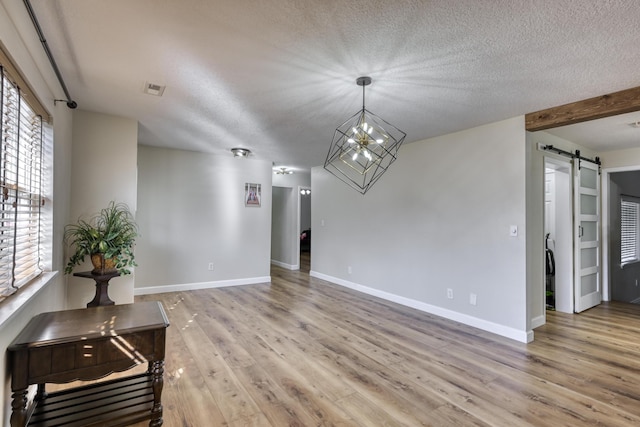 interior space featuring light wood-style flooring, a textured ceiling, an inviting chandelier, and a barn door