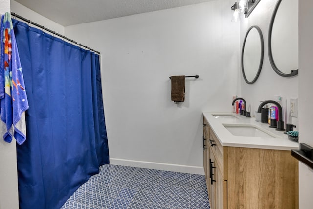 full bath featuring double vanity, a textured ceiling, baseboards, and a sink