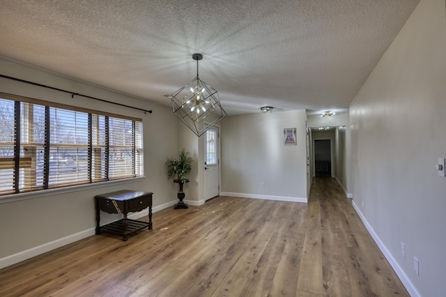 empty room featuring baseboards, a notable chandelier, wood finished floors, and a textured ceiling