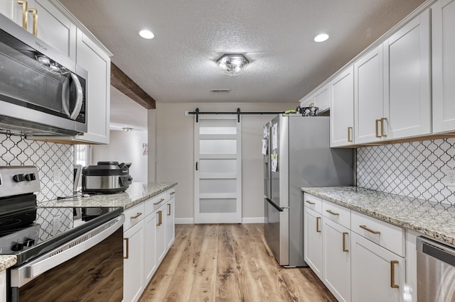 kitchen featuring visible vents, a barn door, appliances with stainless steel finishes, light wood-style floors, and white cabinets