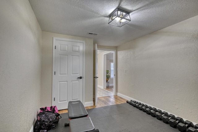 workout area featuring wood finished floors, baseboards, visible vents, a textured ceiling, and a textured wall