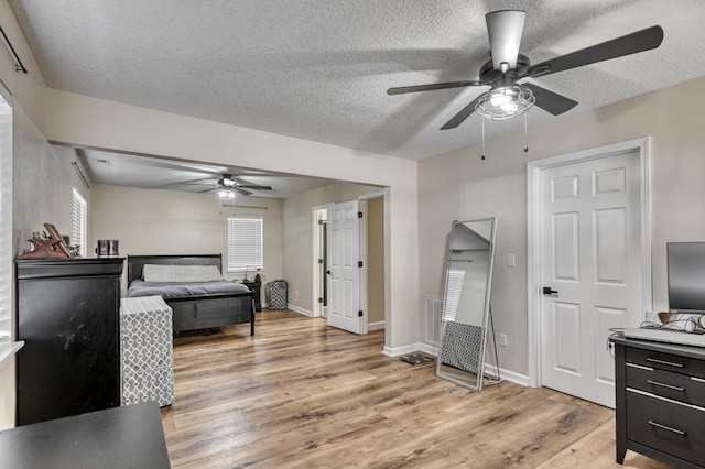 bedroom with a ceiling fan, baseboards, light wood-type flooring, and a textured ceiling