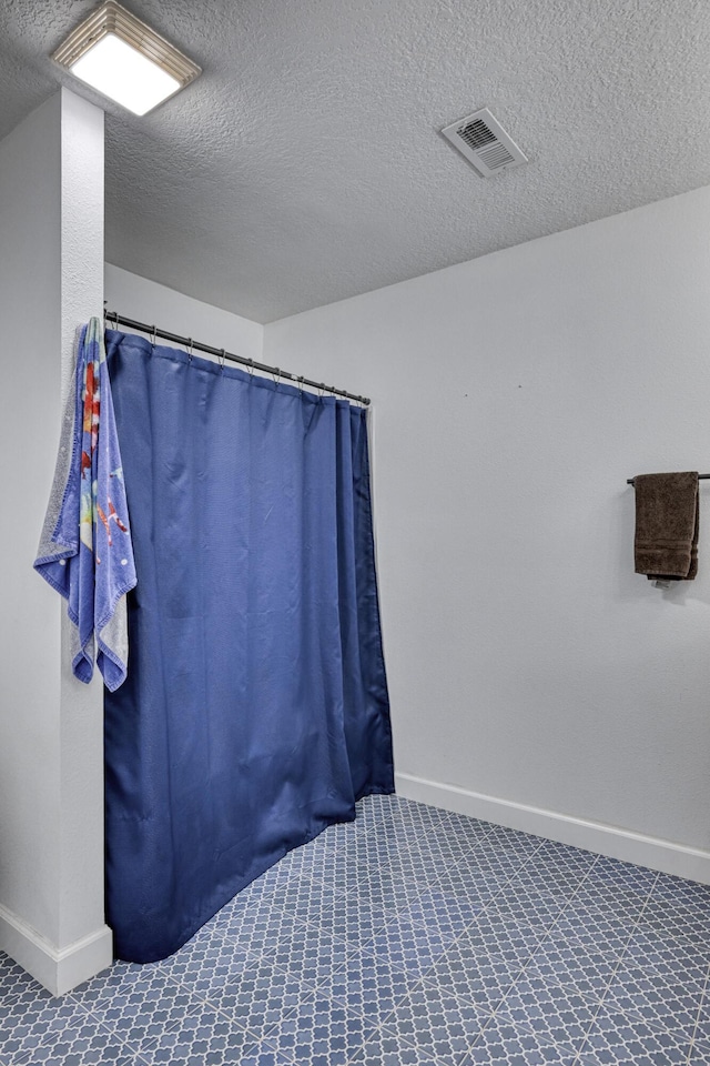 bathroom featuring a shower with curtain, baseboards, visible vents, and a textured ceiling