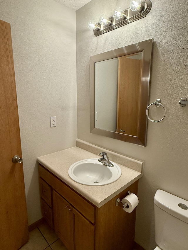 half bathroom with vanity, toilet, a textured wall, and tile patterned flooring