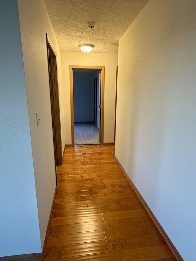 corridor with baseboards, a textured ceiling, and light wood-style flooring