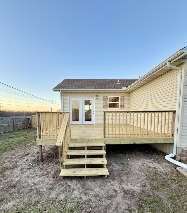 back of house at dusk with a deck, fence, and a shingled roof