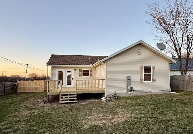 rear view of house featuring a deck, a lawn, roof with shingles, and a fenced backyard