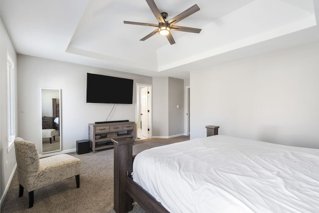 carpeted bedroom featuring a raised ceiling, a ceiling fan, and baseboards