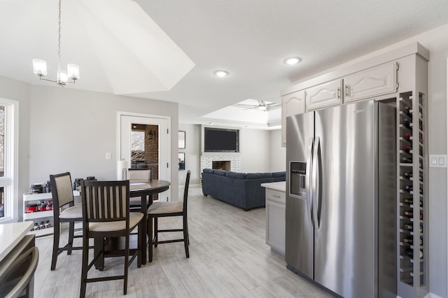 dining room featuring a lit fireplace, recessed lighting, ceiling fan with notable chandelier, light wood-style flooring, and a raised ceiling