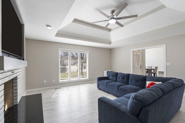 living area with a tray ceiling, a fireplace, light wood finished floors, and ceiling fan