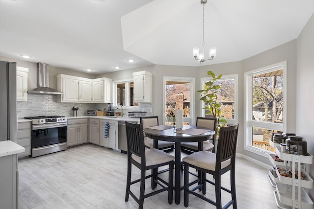 kitchen with wall chimney range hood, tasteful backsplash, light countertops, gas range, and a chandelier