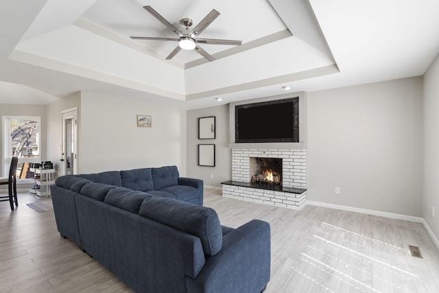 living area featuring a raised ceiling, baseboards, and ceiling fan