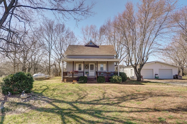 view of front facade with an outbuilding, a front lawn, a detached garage, covered porch, and a shingled roof