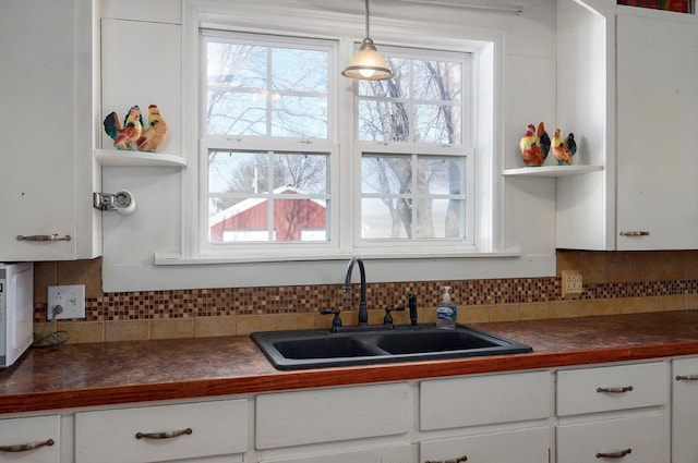 kitchen featuring decorative backsplash, dark countertops, white cabinets, and a sink