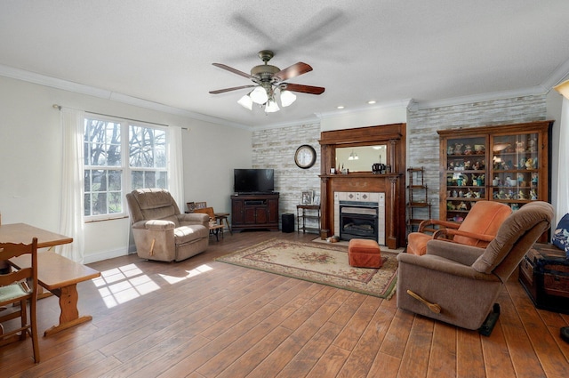 living room featuring ornamental molding, a ceiling fan, a glass covered fireplace, wood finished floors, and baseboards