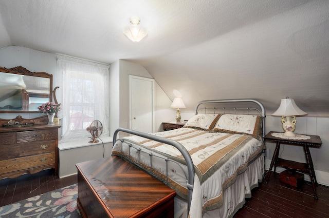 bedroom with a textured ceiling, dark wood-type flooring, and vaulted ceiling