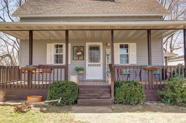 view of exterior entry featuring a porch and a shingled roof