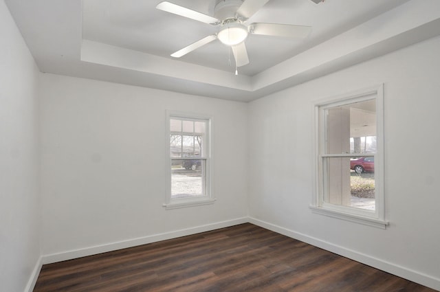 empty room with baseboards, dark wood-type flooring, and a tray ceiling