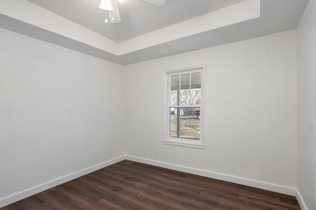 unfurnished room with dark wood-style floors, ceiling fan, a tray ceiling, and baseboards