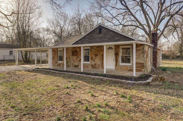 farmhouse-style home featuring stone siding, an attached carport, and a chimney