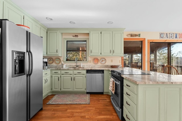 kitchen featuring a sink, a peninsula, green cabinetry, and stainless steel appliances