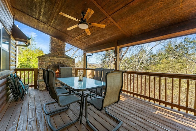 wooden deck with outdoor dining area, an outdoor stone fireplace, and a ceiling fan