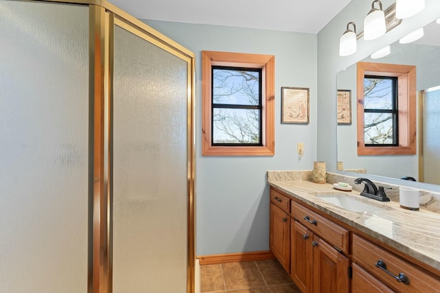 bathroom with baseboards, a healthy amount of sunlight, a stall shower, and vanity