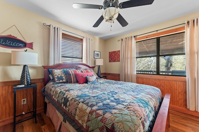 bedroom with wooden walls, wood finished floors, a wainscoted wall, and ceiling fan