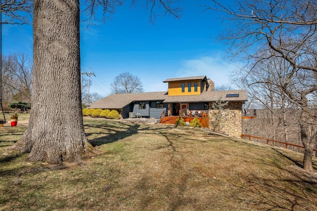 back of house with a lawn, stone siding, and roof with shingles