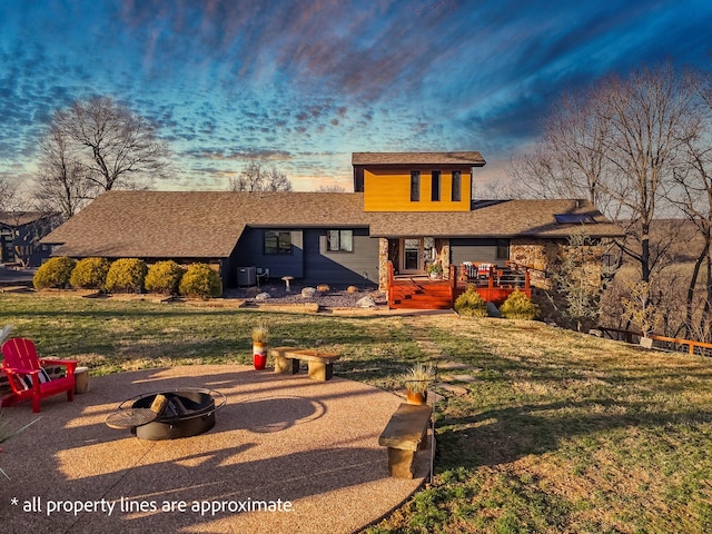 rear view of property with a wooden deck, a lawn, a fire pit, and roof with shingles